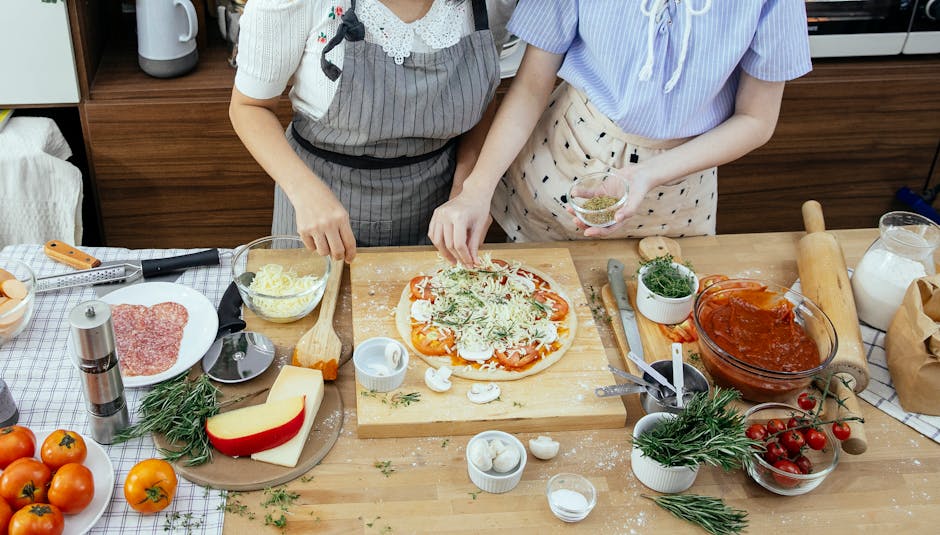 Vista dall'alto di due donne che preparano una deliziosa pizza fatta in casa con ingredienti freschi in una cucina accogliente.