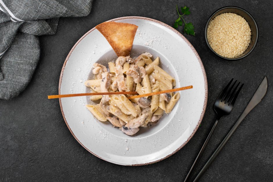 Vista dall'alto di penne cremose ai funghi su piatto elegante con posate.