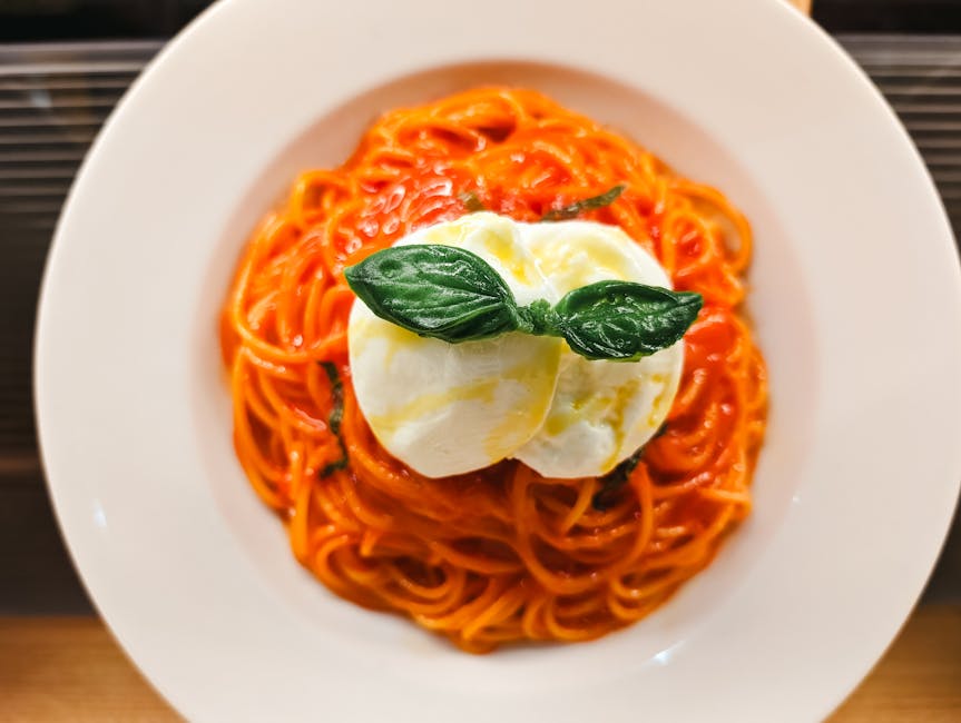 Vista dall'alto di spaghetti con sugo al pomodoro, burrata e foglie di basilico.